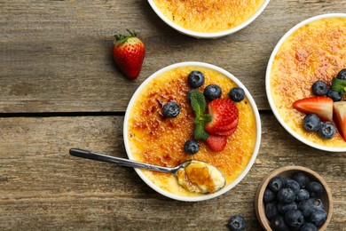 Flat lay composition with delicious creme brulee with berries and mint in bowls on wooden table. Space for text