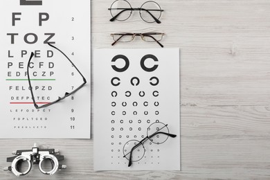 Vision test chart, glasses and trial frame on light wooden background, flat lay. Space for text