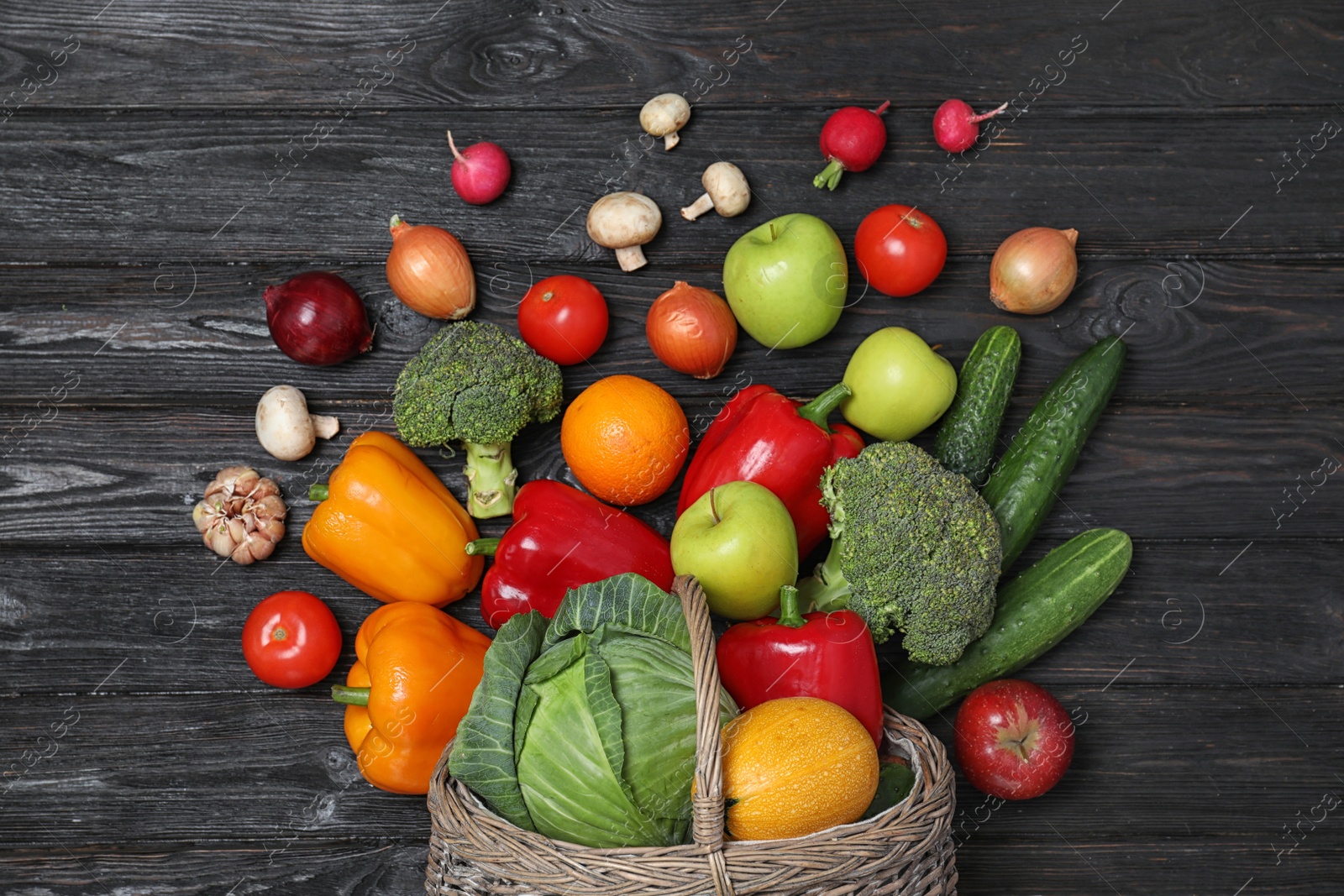 Photo of Basket with scattered fruits and vegetables on black wooden table, flat lay