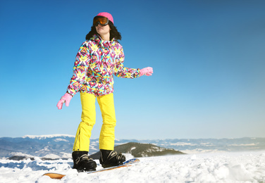 Young woman snowboarding on hill, space for text. Winter vacation