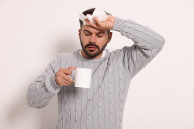 Photo of Sick man with tissue and cup of drink on light grey background. Cold symptoms