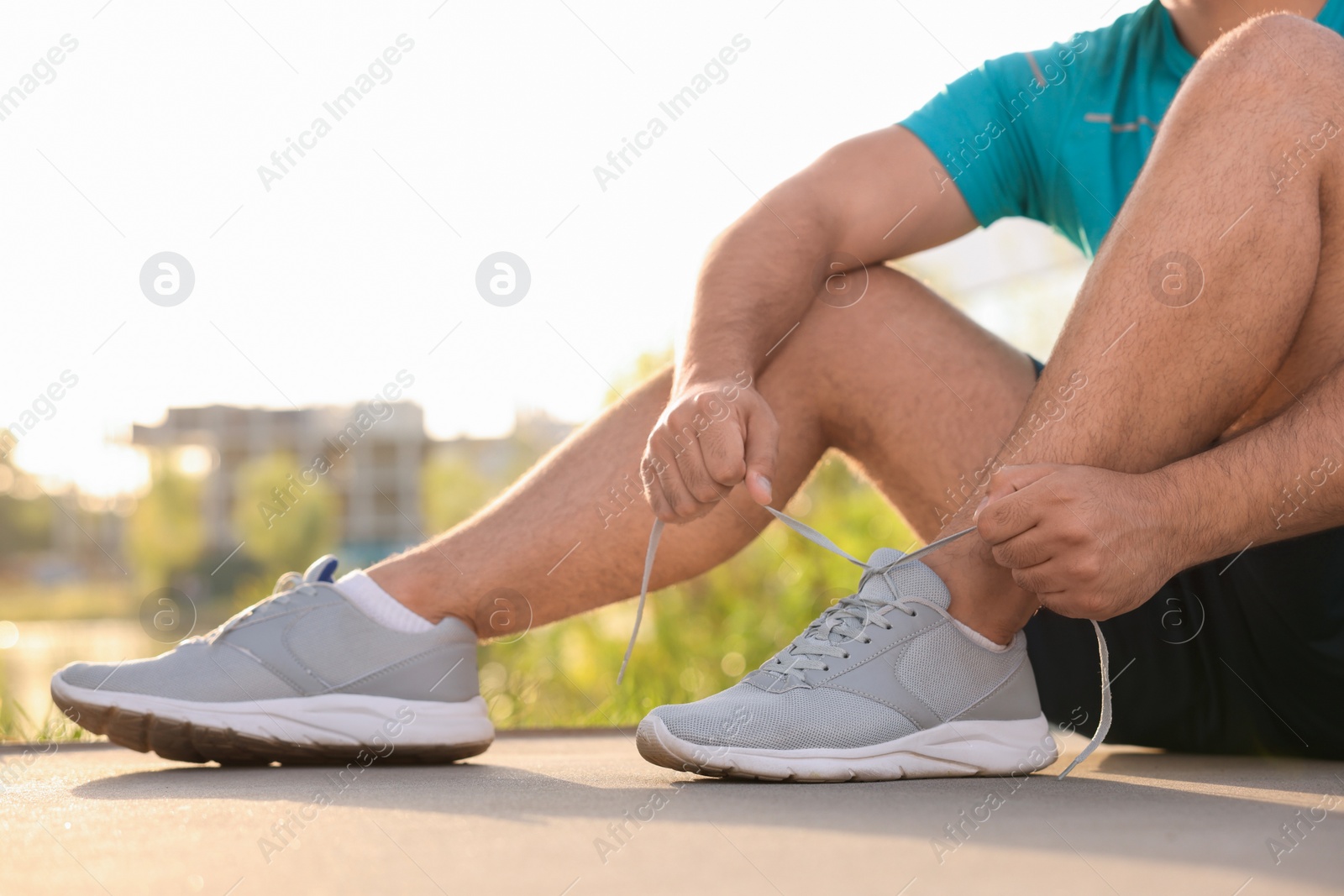 Photo of Man tying shoelaces before running outdoors on sunny day, closeup. Space for text