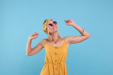 Portrait of smiling hippie woman in sunglasses dancing on light blue background