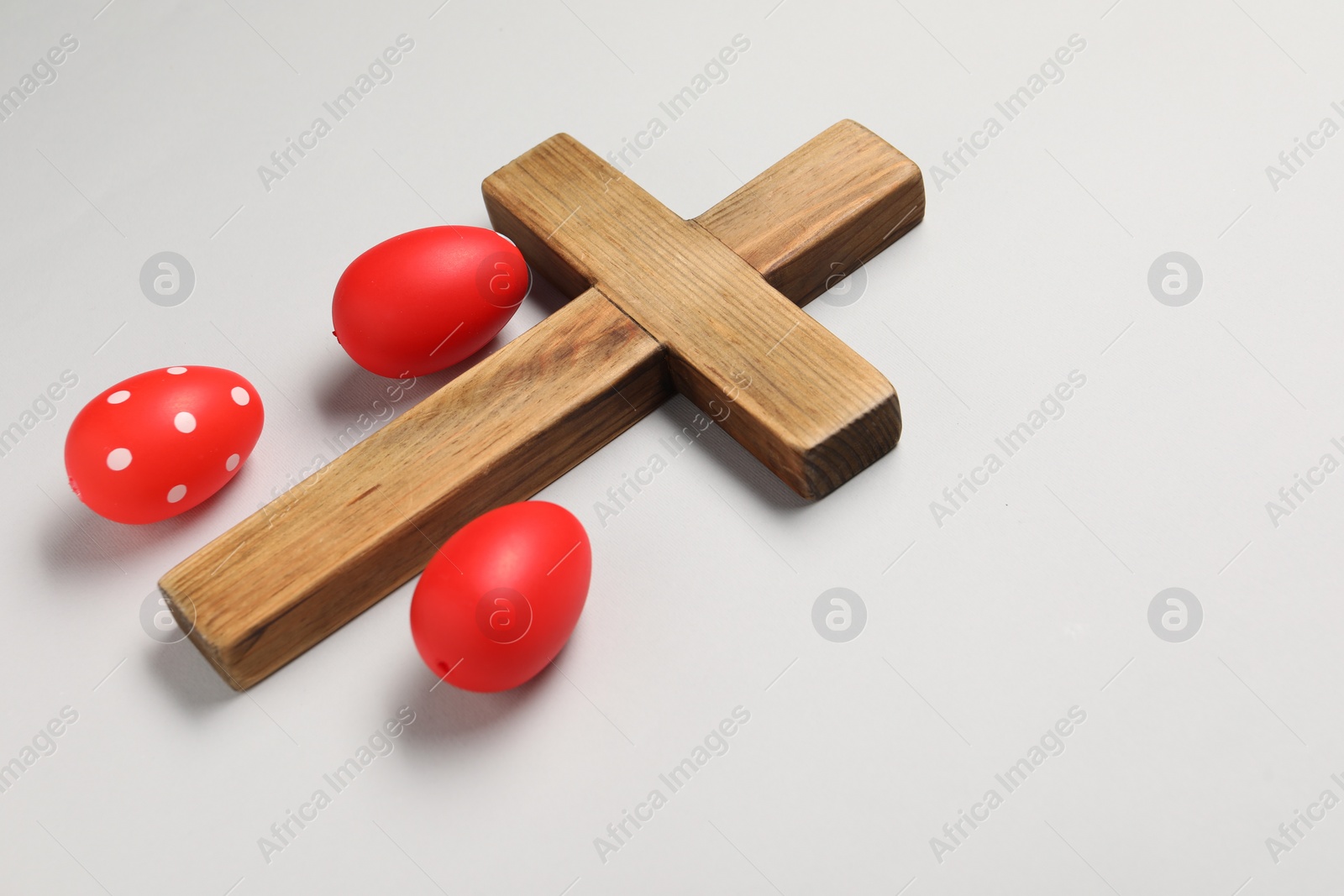 Photo of Wooden cross and painted Easter eggs on light grey background, space for text