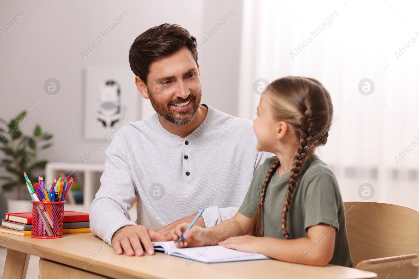 Photo of Dyslexia problem. Father helping daughter with homework at table in room
