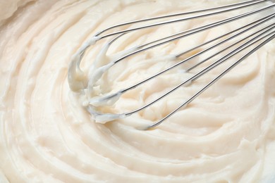 Photo of Whipping beige cream with balloon whisk, closeup view