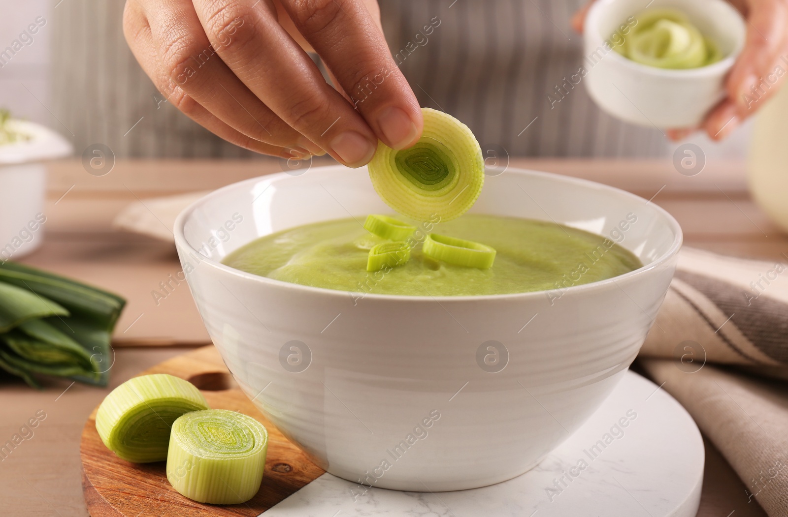 Photo of Woman putting cut leek into bowl of tasty soup at wooden table, closeup