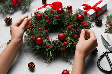 Photo of Florist making beautiful Christmas wreath at grey table, closeup