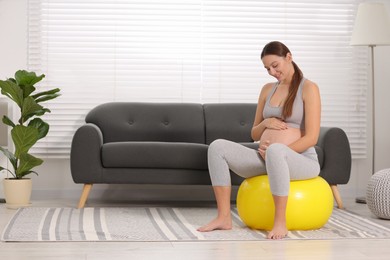 Pregnant woman sitting on fitness ball at home. Doing yoga
