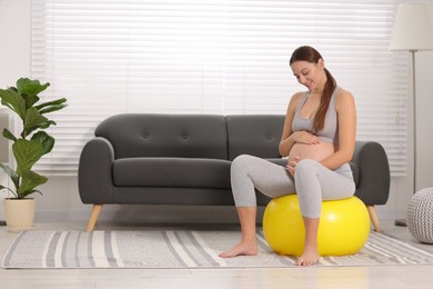 Photo of Pregnant woman sitting on fitness ball at home. Doing yoga