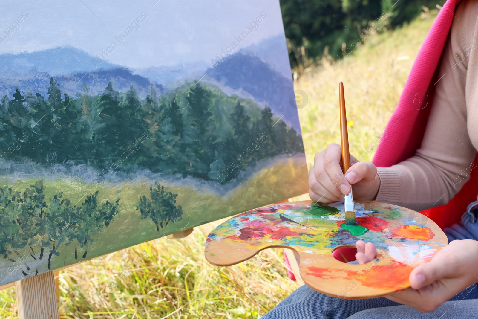 Photo of Young woman drawing on easel with brush outdoors, closeup