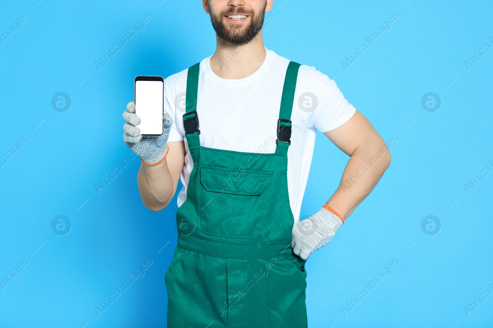 Photo of Professional repairman in uniform showing smartphone on light blue background, closeup