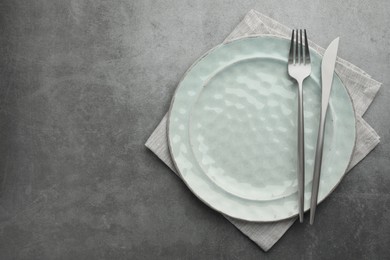 Clean plate, cutlery and napkin on grey table, top view. Space for text