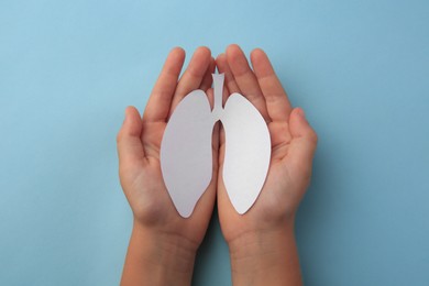 Photo of Child holding paper human lungs on light blue background, top view
