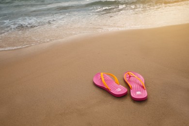 Photo of Bright pink beach slippers on sand near sea, space for text