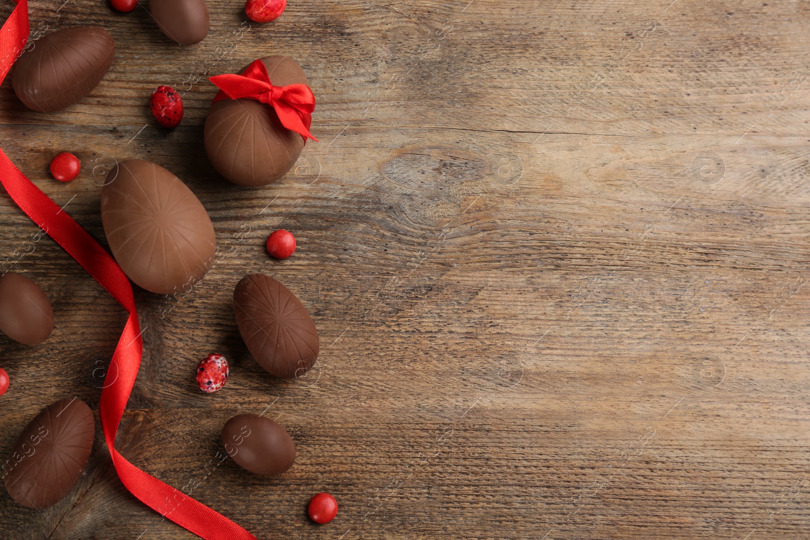 Photo of Sweet chocolate eggs and candies on wooden table, flat lay. Space for text