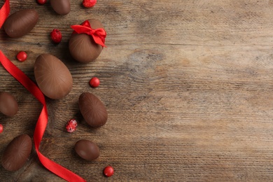 Sweet chocolate eggs and candies on wooden table, flat lay. Space for text