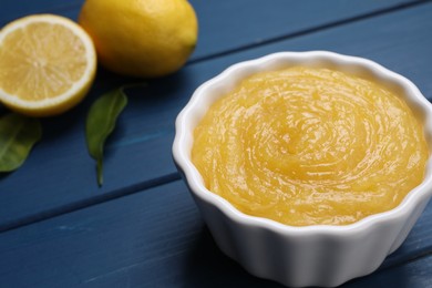 Delicious lemon curd in bowl and fresh citrus fruits on blue wooden table, closeup