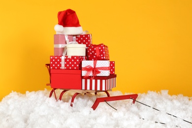 Sleigh with presents and Santa hat in artificial snow on yellow background