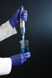 Photo of Laboratory analysis. Scientist dripping sample with micropipette into beaker on dark background, closeup