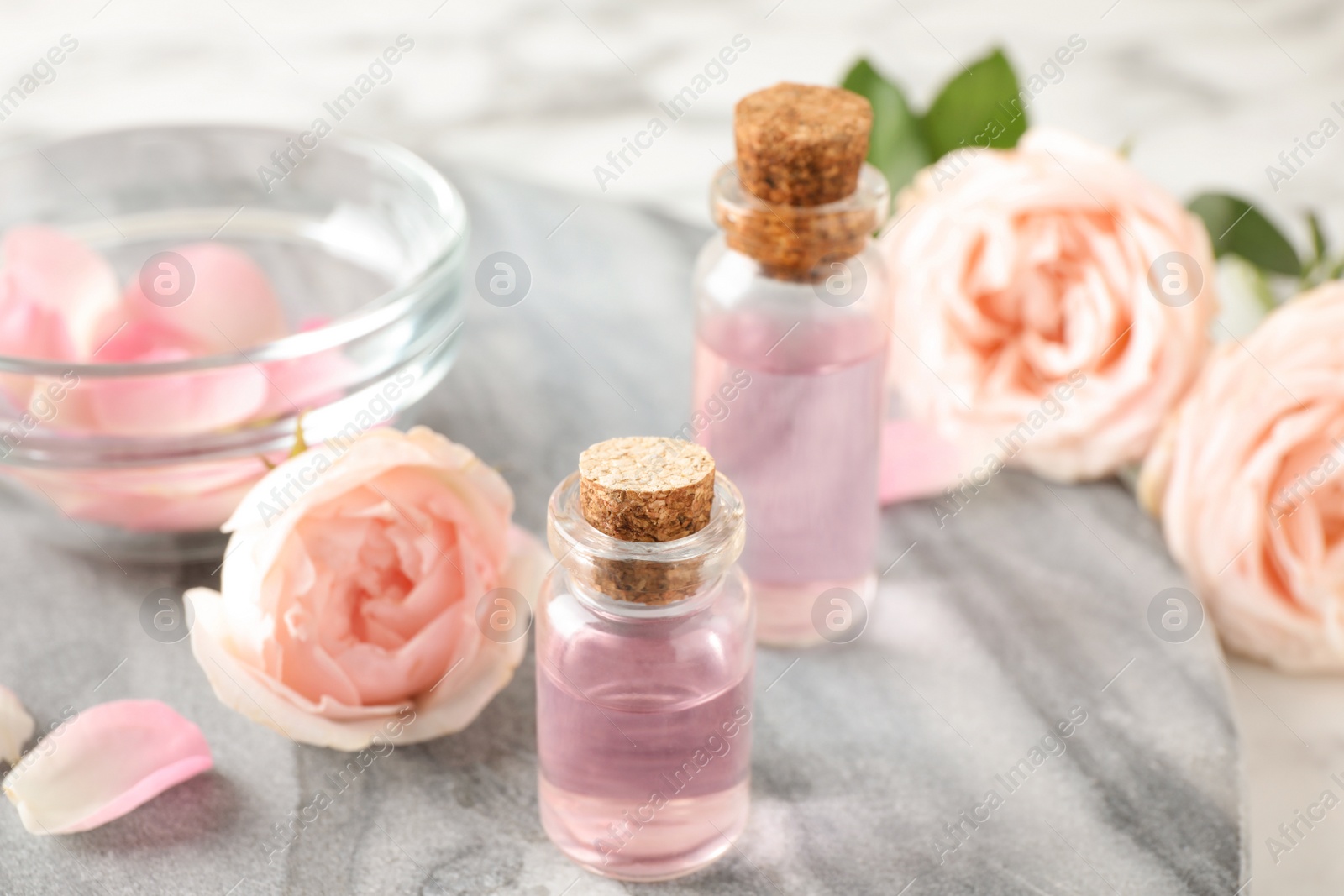 Photo of Bottles with rose essential oil and flowers on stone board