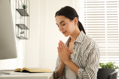 Photo of Beautiful young woman praying over Bible at desk