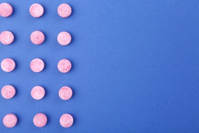 Many pink vitamin pills on blue background, flat lay. Space for text