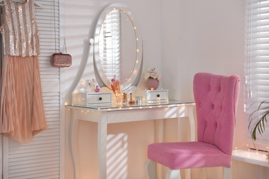 Elegant dressing table with lights and pink chair in stylish room interior