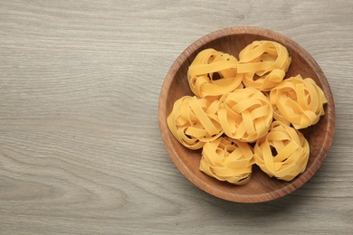 Photo of Raw tagliatelle pasta in bowl on light grey wooden table, top view. Space for text