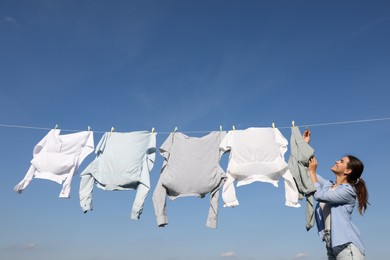 Photo of Woman hanging clothes with clothespins on washing line for drying against blue sky outdoors
