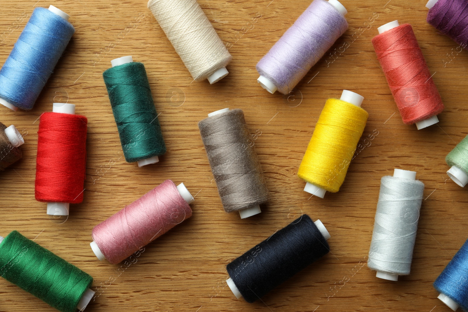 Photo of Many colorful sewing threads on wooden table, flat lay