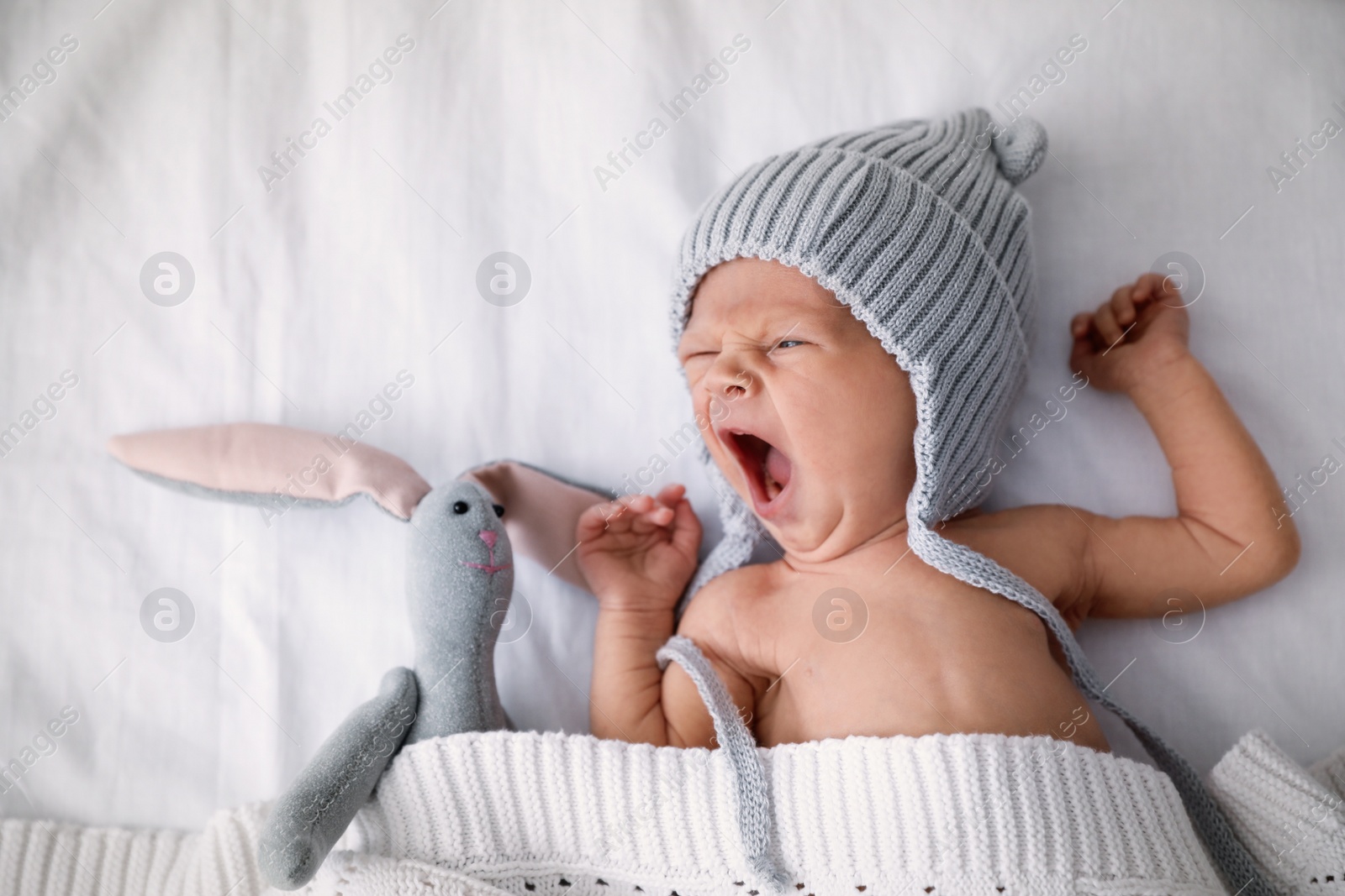 Photo of Adorable newborn baby in knitted hat with toy bunny on bed, top view