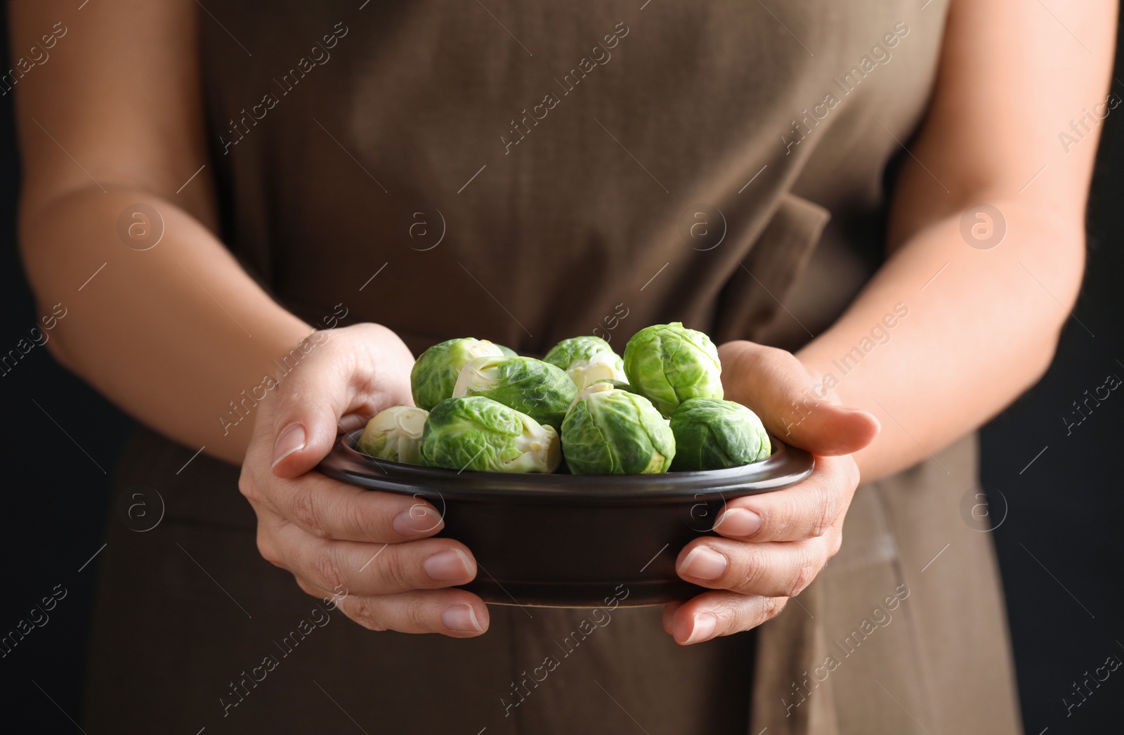 Photo of Woman holding bowl with Brussels sprouts on black background, closeup