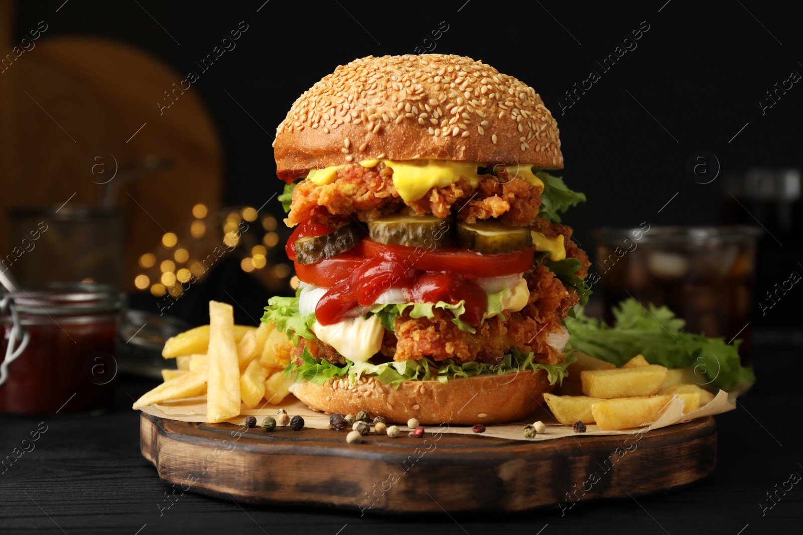 Photo of Delicious burger with crispy chicken patty and french fries on black wooden table