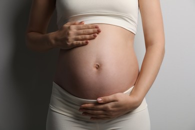 Photo of Pregnant young woman touching belly on light background, closeup