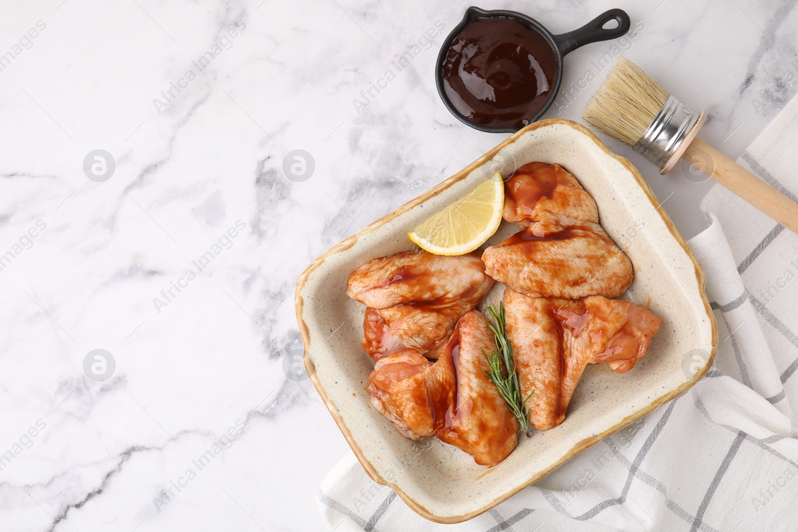 Photo of Fresh marinade, basting brush, raw chicken wings, rosemary and lemon on white marble table, flat lay. Space for text