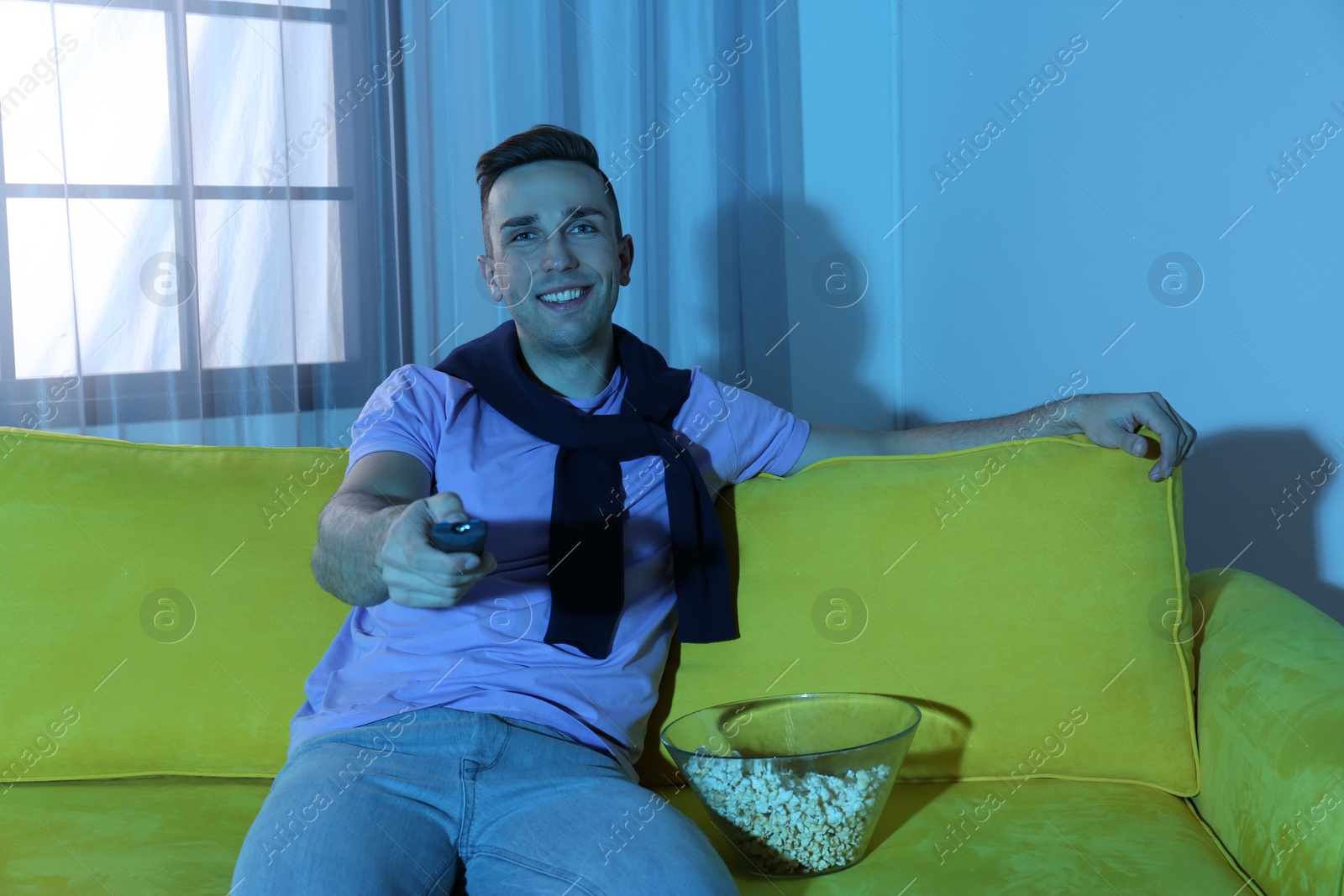 Photo of Handsome young man watching TV on sofa at home