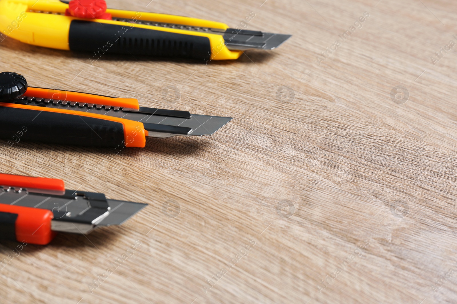 Photo of Three utility knives on wooden table, closeup. Space for text