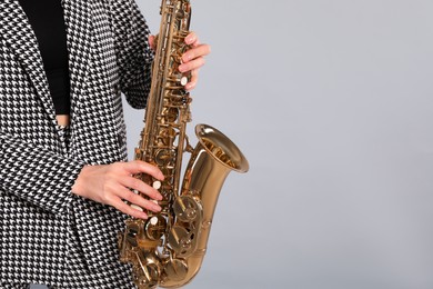 Photo of Woman in elegant suit with saxophone on grey background, closeup. Space for text