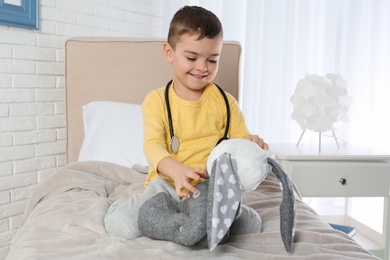 Photo of Cute child playing doctor with stuffed toy at hospital