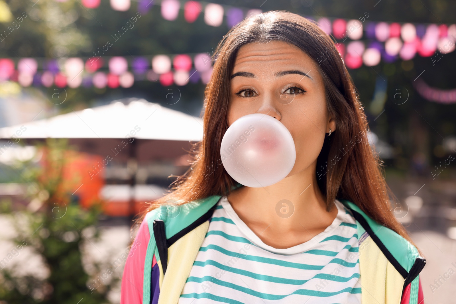 Photo of Beautiful young woman blowing chewing gum on city street outdoors