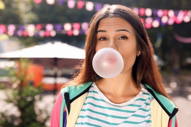 Photo of Beautiful young woman blowing chewing gum on city street outdoors