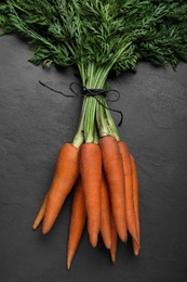Photo of Bunch of tasty raw carrots on black slate table, top view