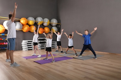 Photo of Cute little children and trainer doing physical exercise in school gym. Healthy lifestyle