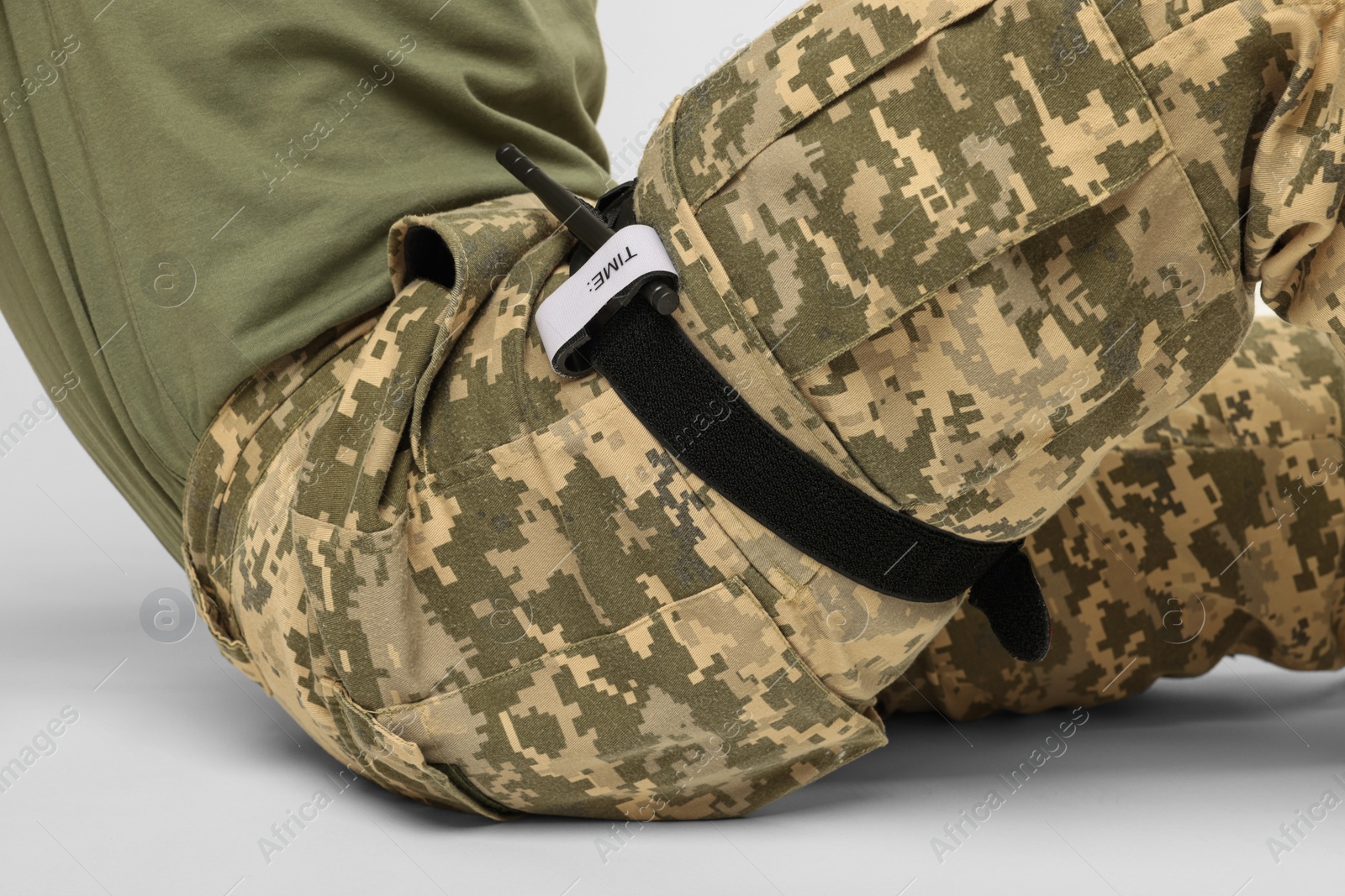 Photo of Soldier in military uniform with medical tourniquet on leg against white background, closeup