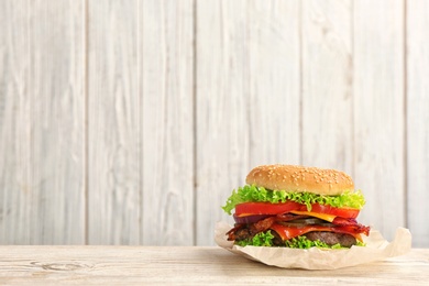 Photo of Tasty burger with bacon on table against wooden background. Space for text