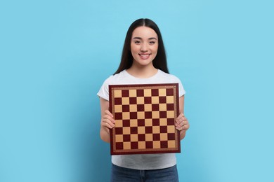 Photo of Happy woman with chessboard on light blue background