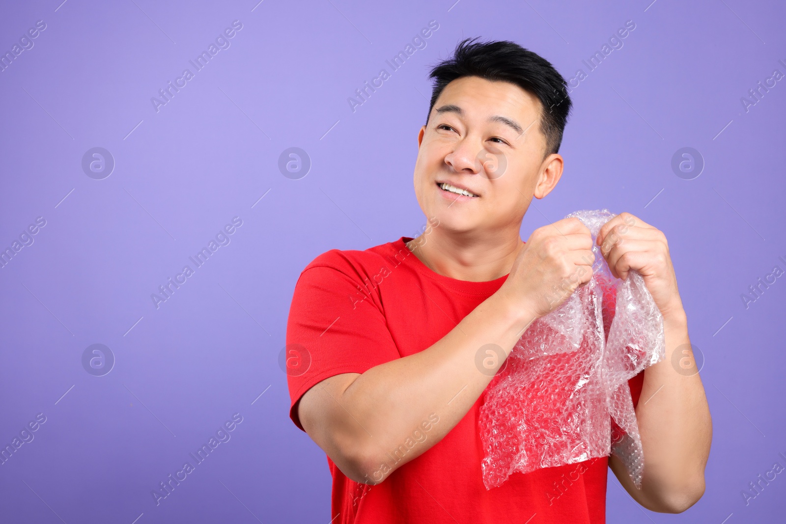 Photo of Happy asian man with bubble wrap on purple background. Space for text