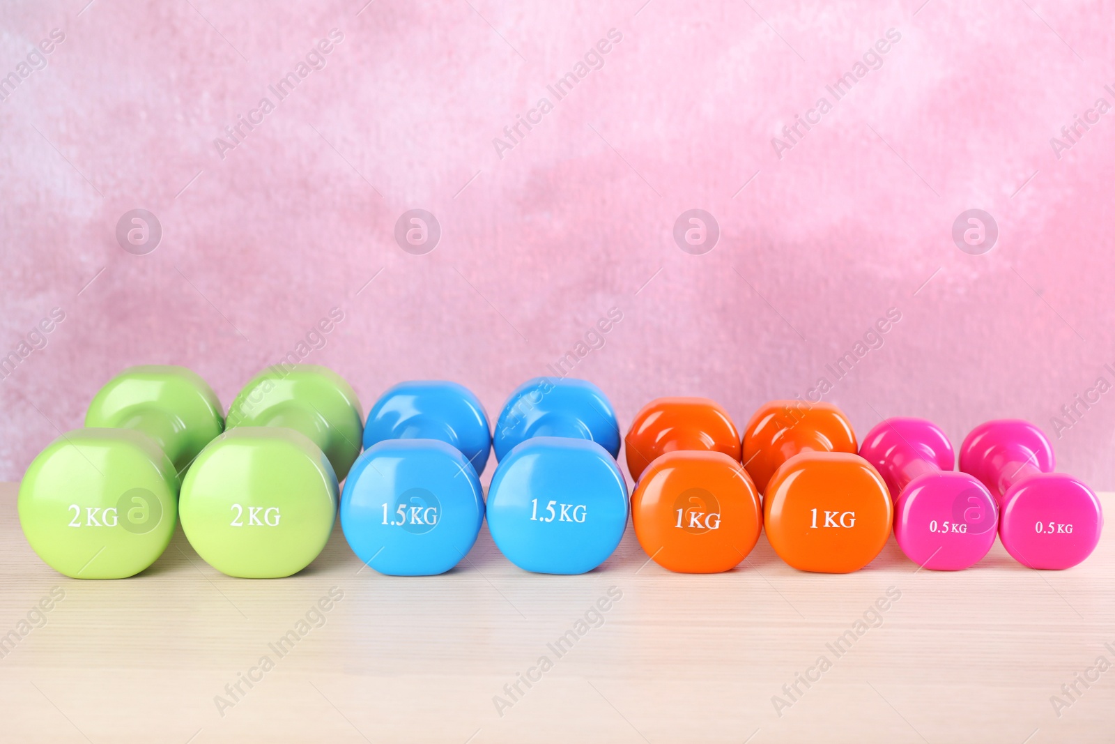 Photo of Many dumbbells on table against color background. Fitness equipment