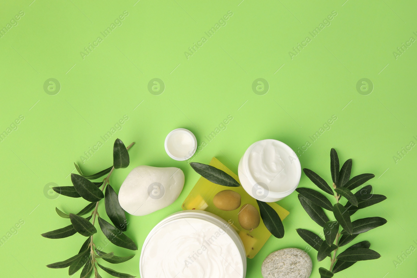 Photo of Different cosmetic products with olives and stones on light green background, flat lay. Space for text